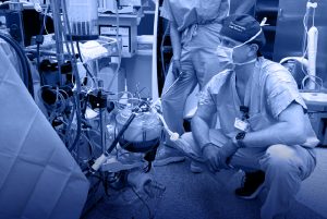 Perfusionist operating heart-lung machine during cardiovascular surgery in a hospital operating room, surrounded by complex medical equipment, wires, and monitors