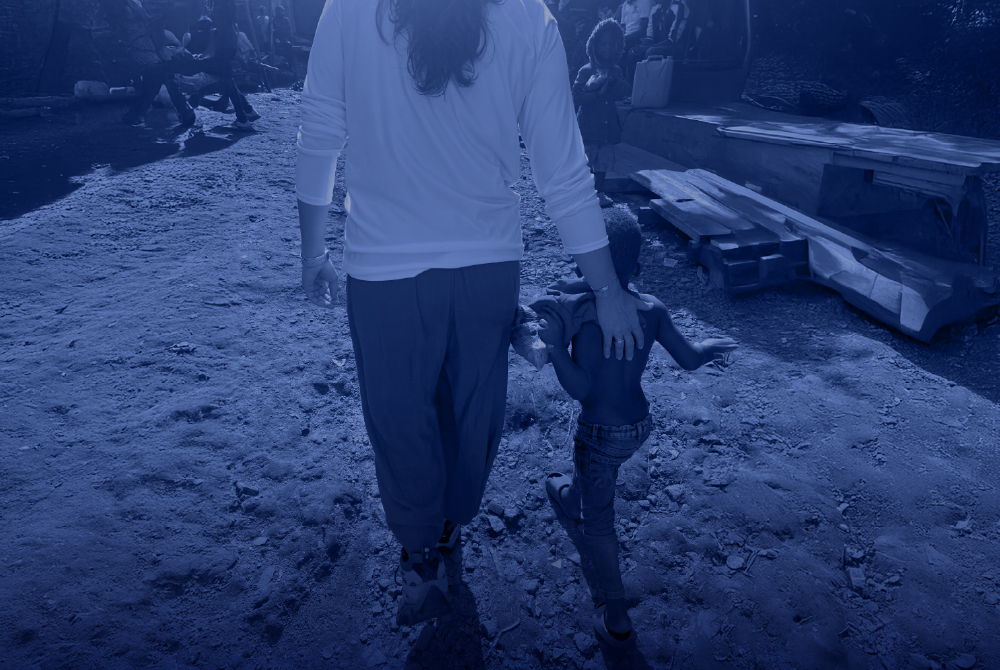 An adult and a child walk hand in hand through a rural area in Uganda, surrounded by makeshift structures and local community members.