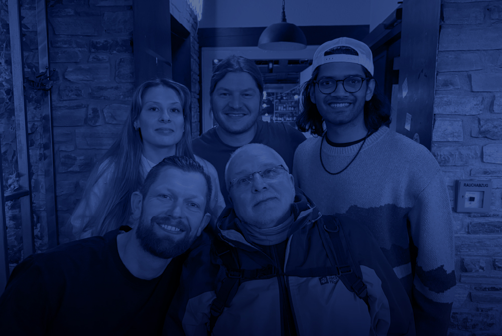 A group of perfusionists smile for a photo during a visit to Germany, standing together in a warmly lit indoor space with brick walls.