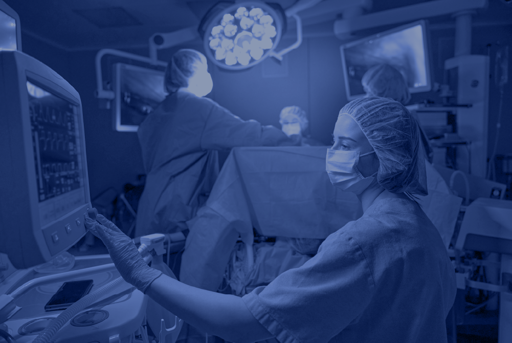 Healthcare professional in surgical attire operating monitoring equipment during a procedure, representing clinical leadership and teamwork in the operating room.