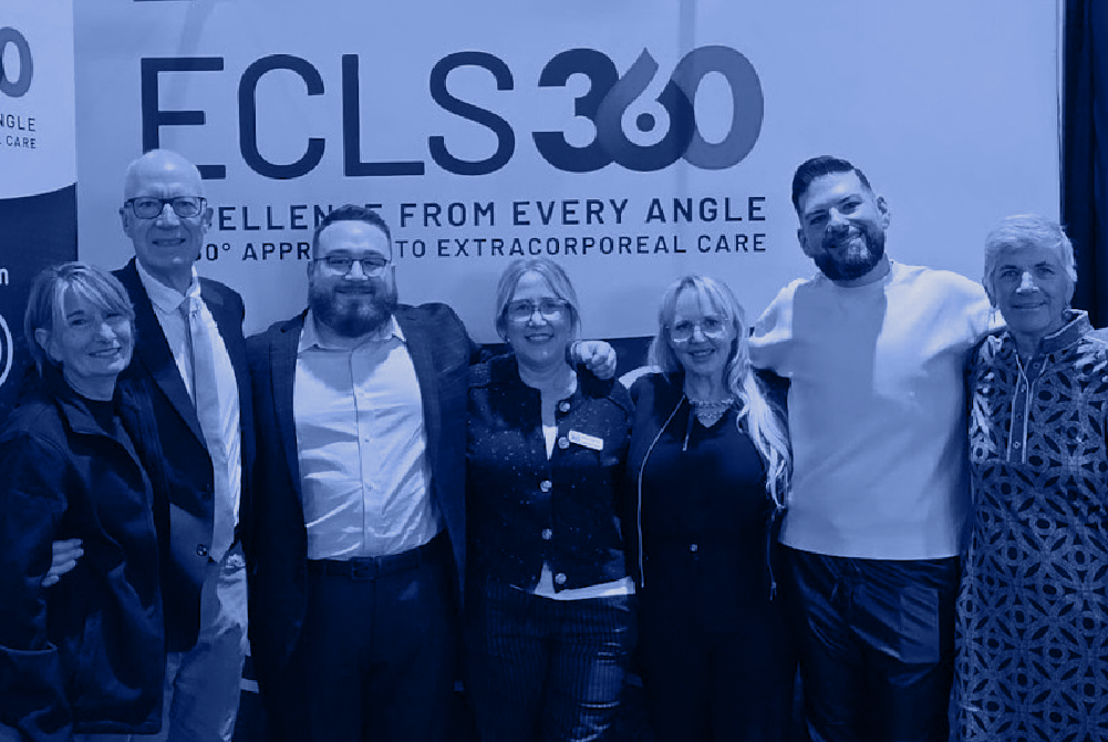 Group of ECMO and extracorporeal care professionals standing together in front of an ECLS360 conference display.