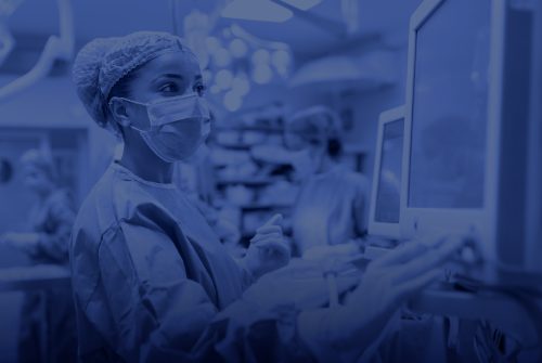 A surgical team works in a hospital operating room, with a masked and gloved medical professional monitoring vital signs on a screen.